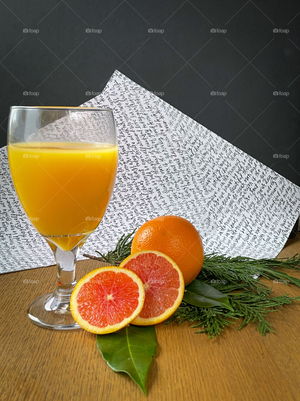 Glass of orange juice with sliced oranges and green foliage. 