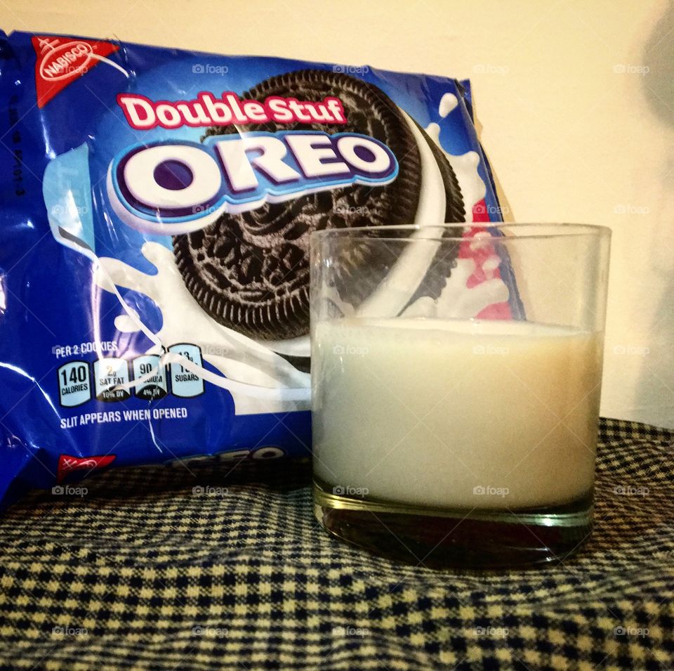 A glass of milk in front of a package of Double Stuf Oreos on top of a checkered tablecloth. 