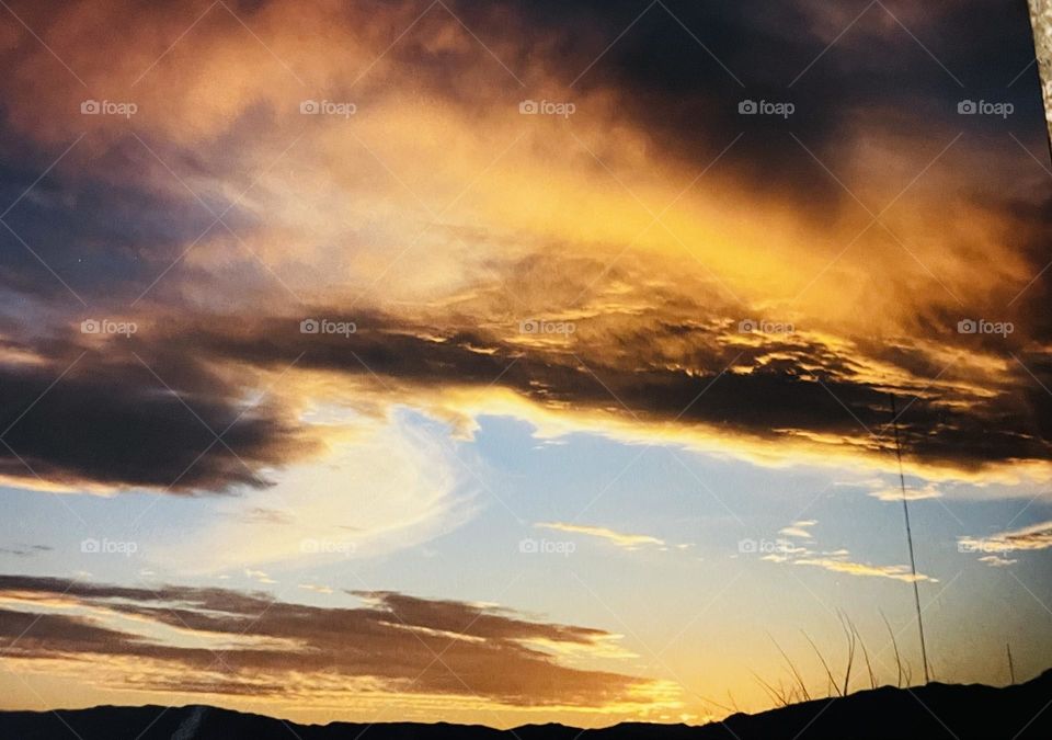 A sunset with yellow clouds above and mountains below. 