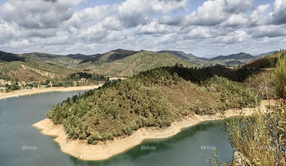 Sunshine and fluffy white clouds over the Rio Zêzere and mountainous landscape