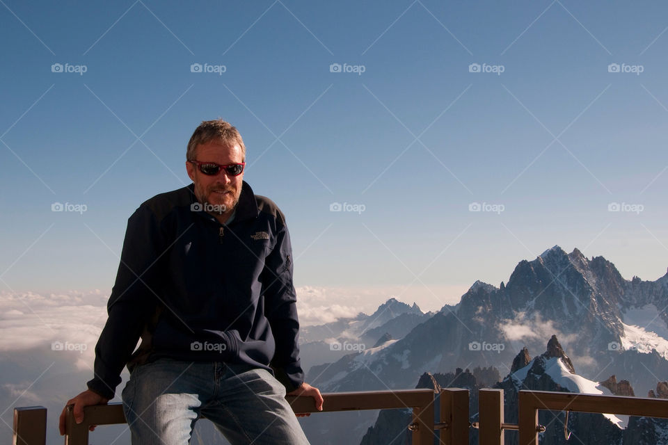 Man sits on the railing in front of the snowcapped mountains