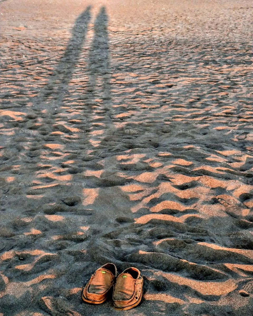 The shadows on the beach at sunset and a pair of shoes. two persons left in the twilight of the last life, that is maybe happy or not happy, but we should do our best in our life. this scenery gave me food for thought.