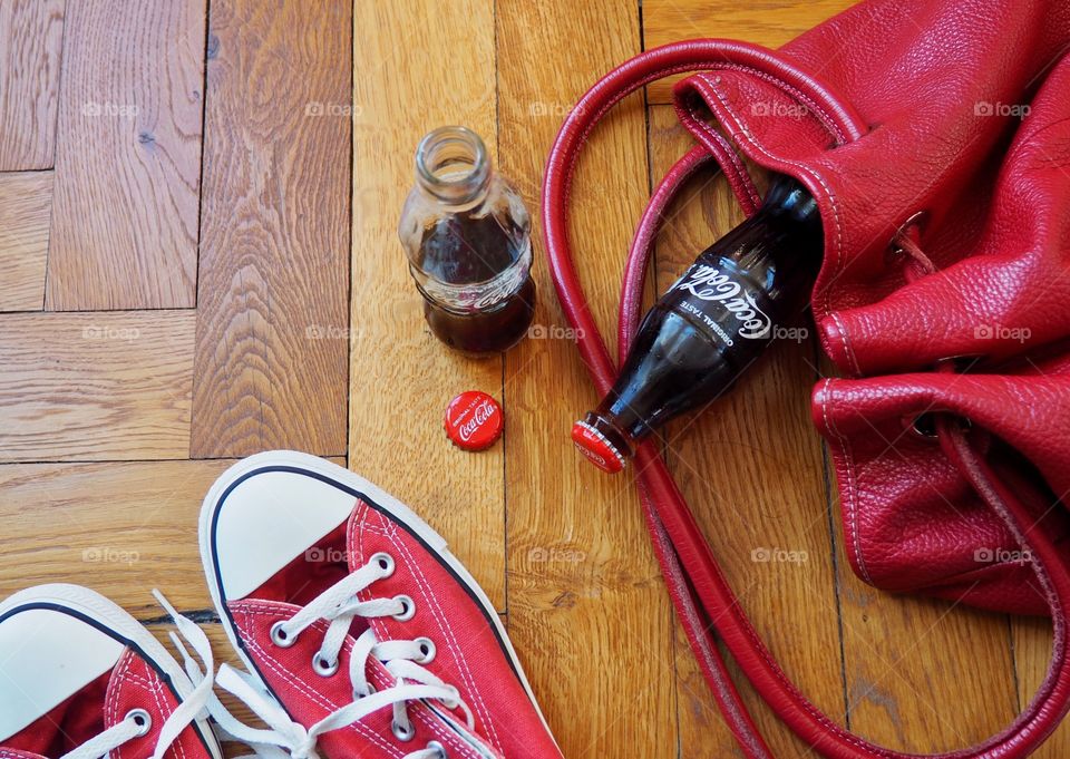 Coca Cola bottles on hardwood floor with red sneakers and red leather bag.