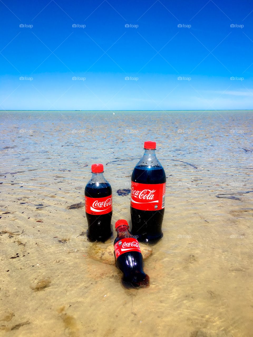 A “family” of three at the beach: represented by the three sizes of Coca Cola. The vivid red labels work well against the tropical blue and the Beach is one of the best places I know of to quench my thirst with Coke!