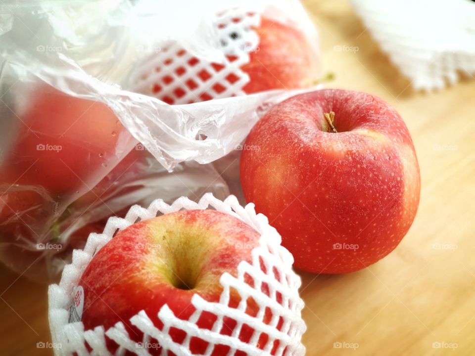 Fresh imported apples from a supermarket come with SINGLE-USE PLASTICS grocery bag and fruit foam net. Environmentalism & Plastic Awareness.
