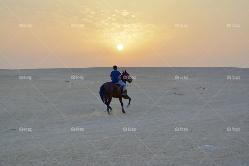 A man riding a horse in desert towards sunset 