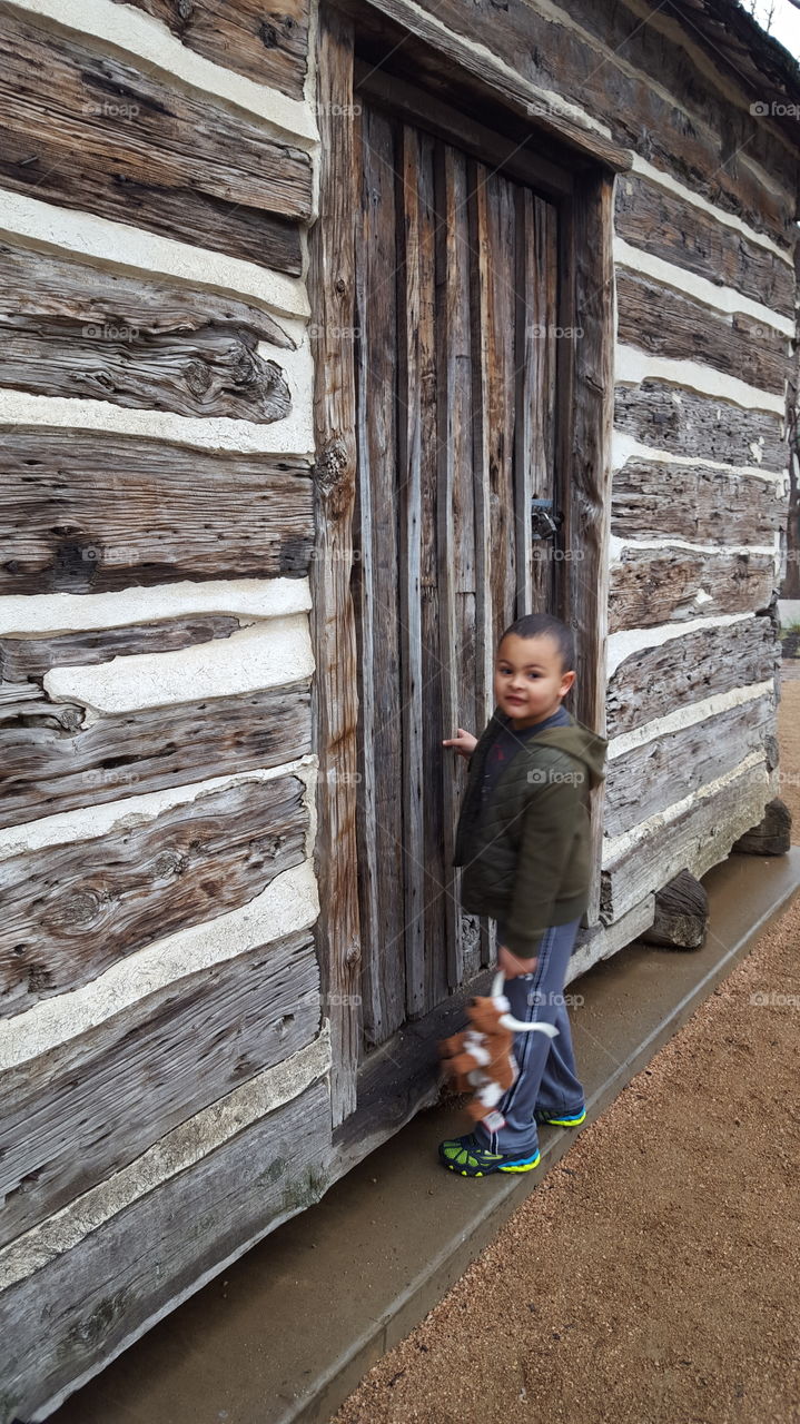 A little boy standing near wooden house with toy
