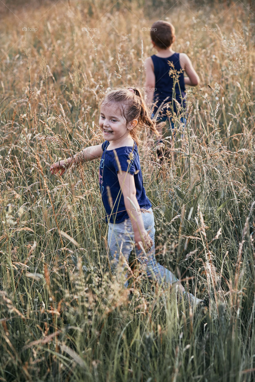 Little happy smiling kids playing in a tall grass in the countryside. Candid people, real moments, authentic situations