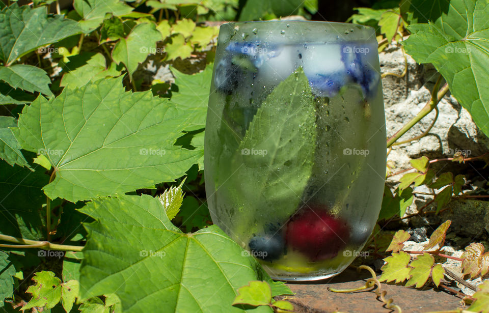 Refreshing flavored water with fresh mint herbs, cherries and summer berries on stones in garden for garden party or entertaining summer beverage 