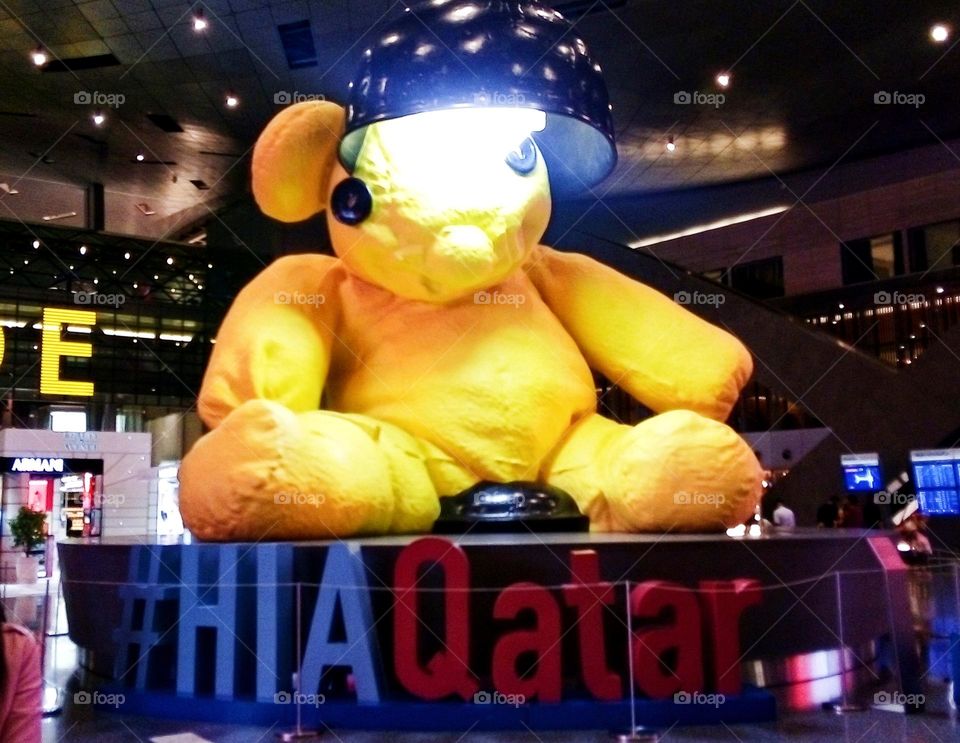 An iconic gigantic sculpture Yellow Lamp Teddy Bear made of bronze sitting and welcoming passengers at Hamad International Airport, Qatar.