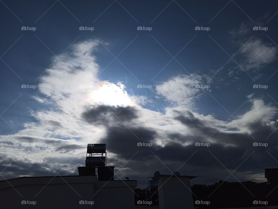 A photo of the dark cloudy sky with sun behind clouds. From the house roof
