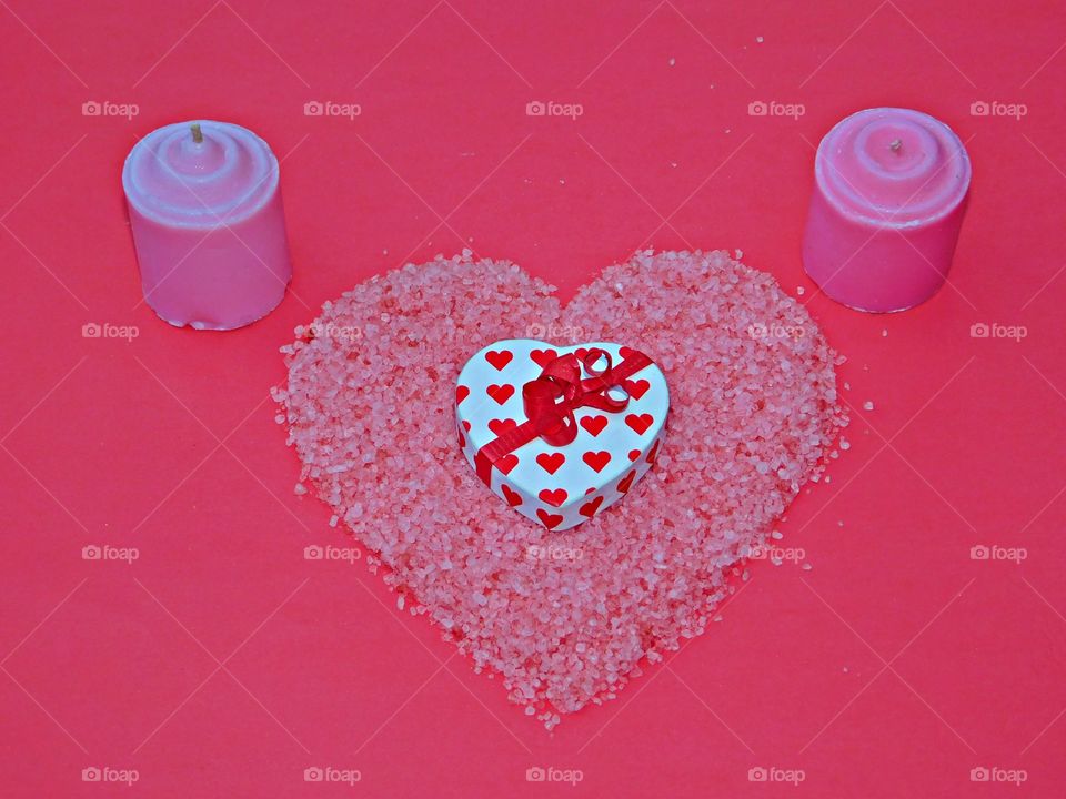 
A flat lay is simply a photo of objects arranged on a flat surface, captured from directly above. Flat lay of a heart decorated box inside a red heart shaped salt design with a candle backdrop