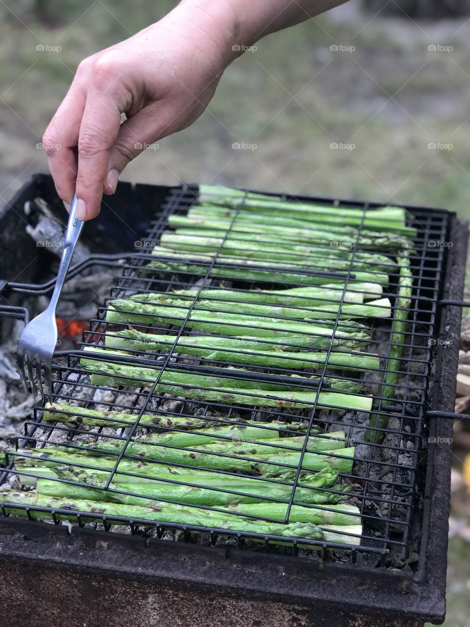 man's hand with fork cooks green asparagus on the grill