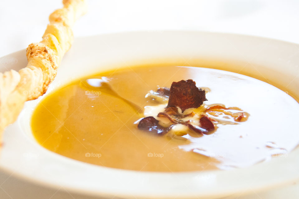 A bowl of warm soup with beet crisps and a twist of cheese bread