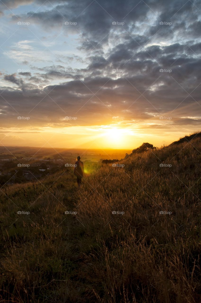 girl walking in golden fields of Glastonbury hill during sunset