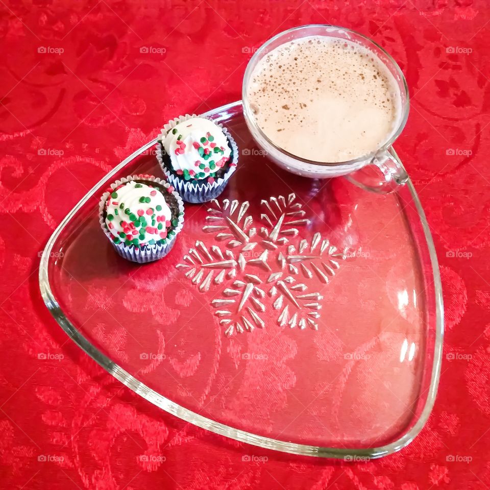 Christmas cupcakes on a snow flake plate against a red background with a cup of hot chocolate