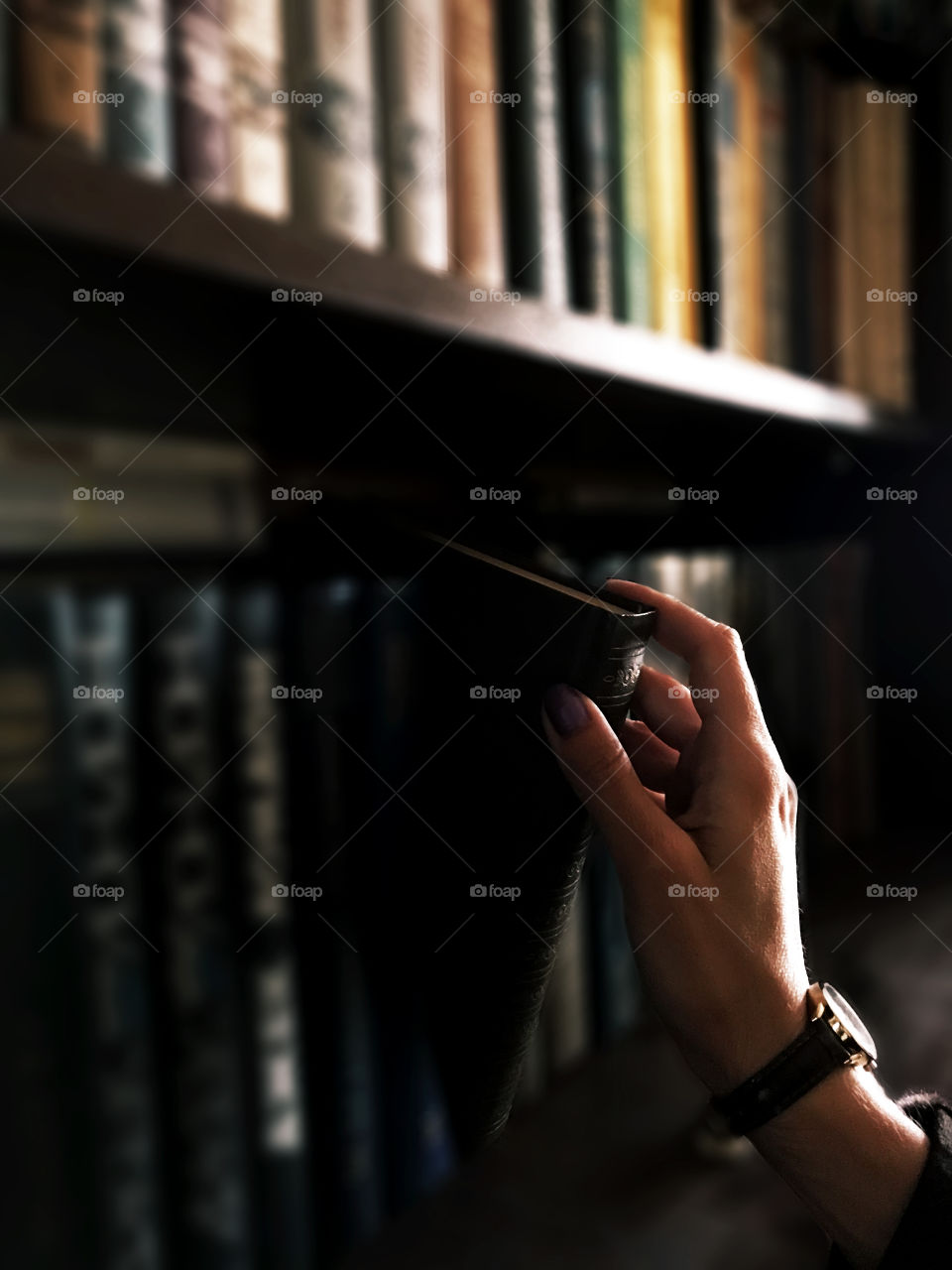 Female hand taking a book from the bookshelf 