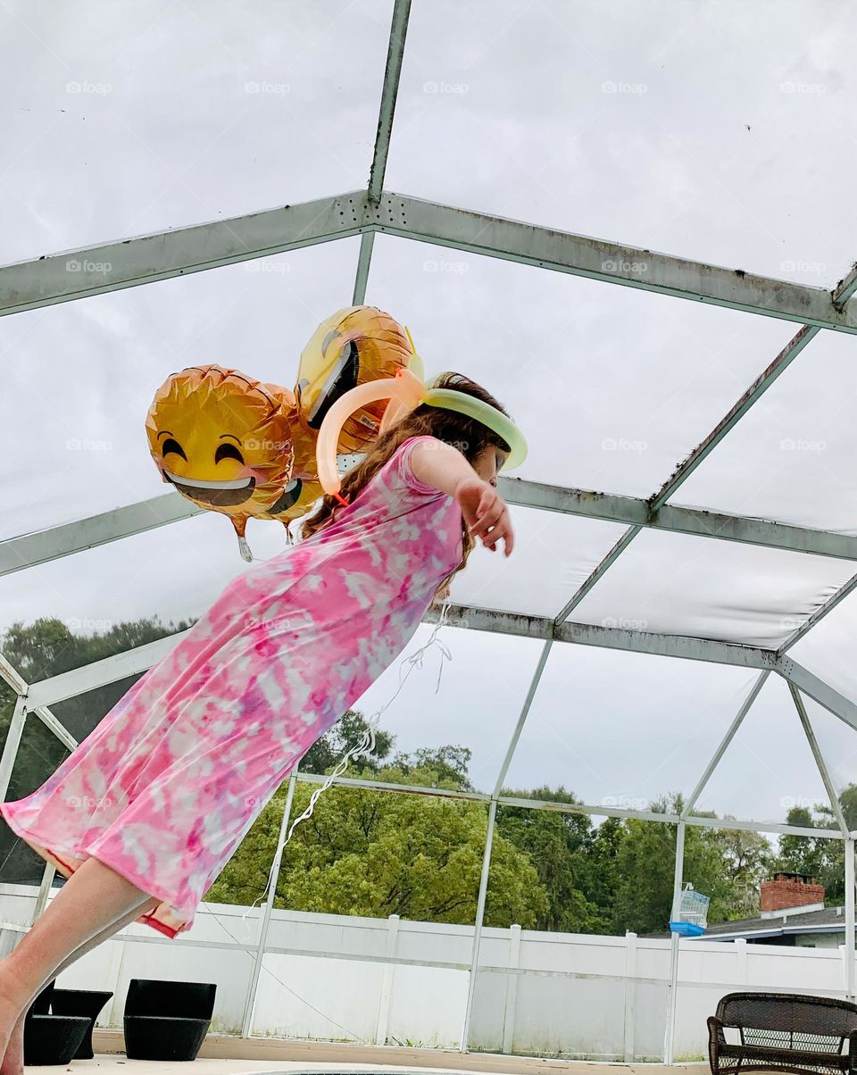 Smiley Faces Helium Balloons Seem To Pull The Girl Up In The Air While She Jumps In The Water With It In The Pool.