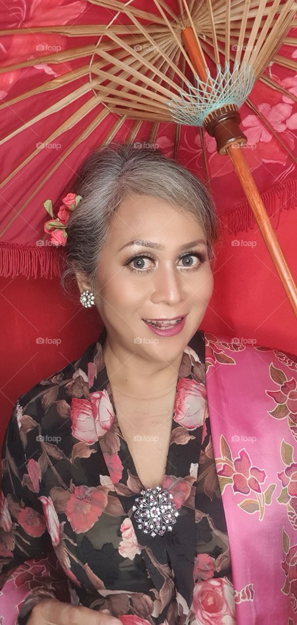 A woman wearing traditional Javanese,Indonesian clothes called kebaya is smiling while holding an umbrella