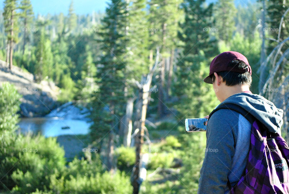 man, boy, taking a photo, while hiking, of the lake stream, in a beautiful view