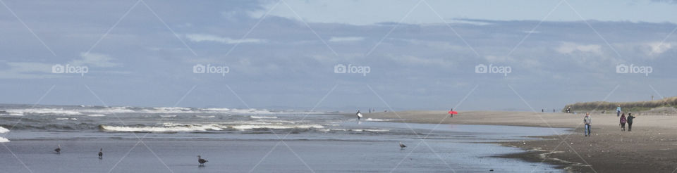 City Beach at Ocean Shores Washington. Mid afternoon crowd. Two surfers heading in shore after a full day of surfing.