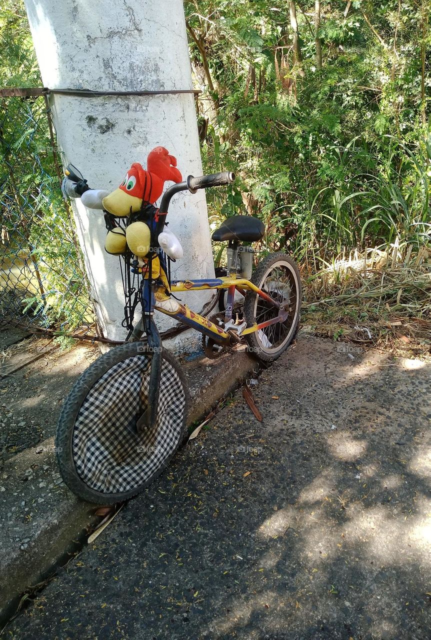 A bicycle with a soft toy left by the entrance of a wood bridge
