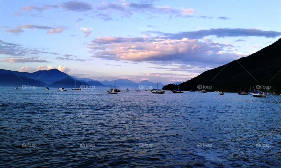 Belas águas, navios e lanchas em praia brasileira em fim de tarde.