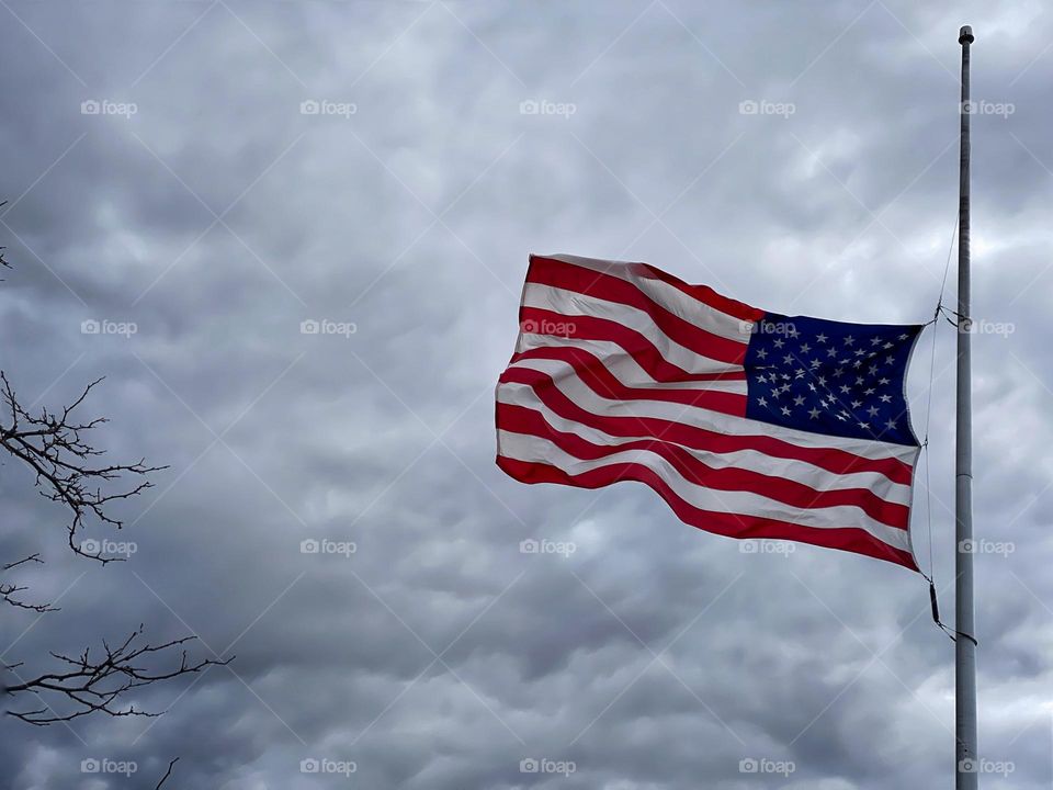 American flag flying at half-mast against a grey, cloudy sky