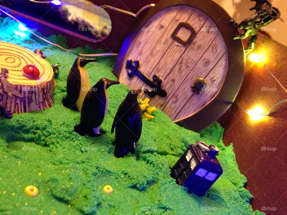 Penguins and a tiny TARDIS wait at the door of a hobbit hole while a dragon perches on the door.