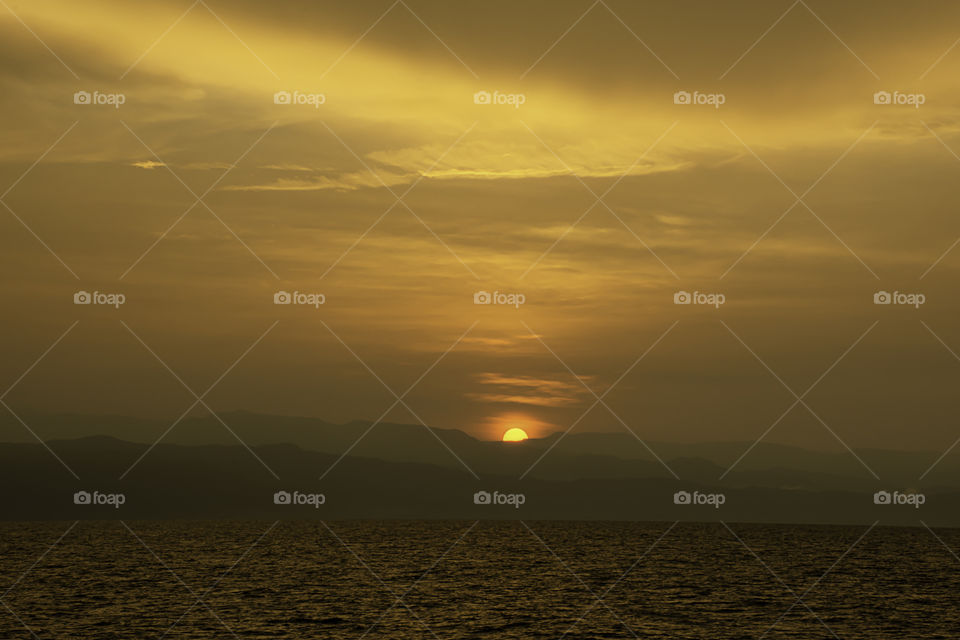 Golden light of sunrise behind the mountains and the sea.