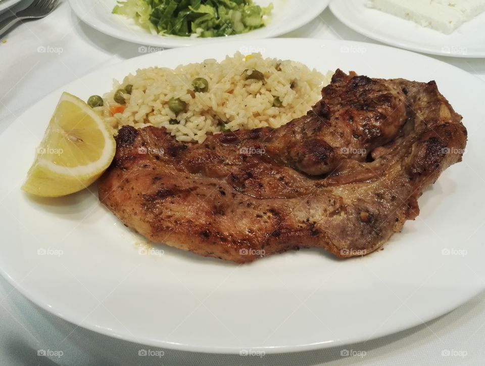 steak chop, rise with vegetables and lemon on plate closeup