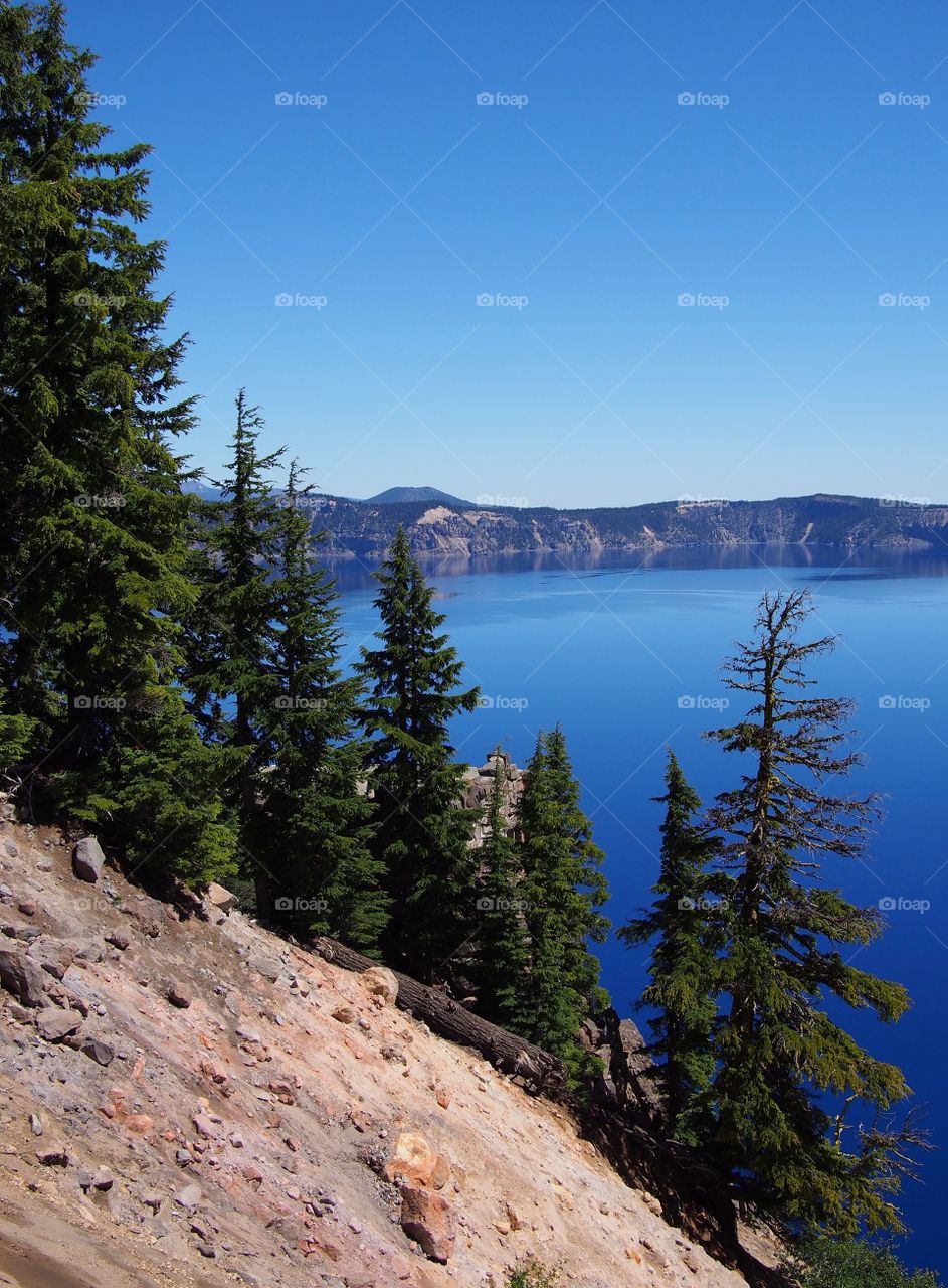 The rugged rim reflect in the stunning rich blue waters of Crater Lake in Southern Oregon on beautiful sunny summer morning. 