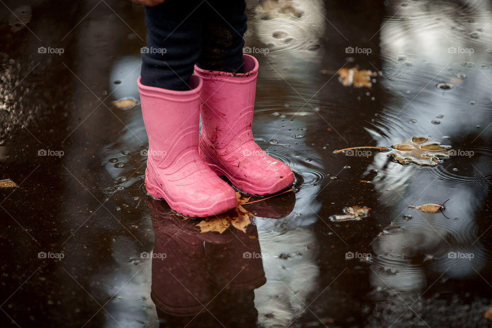 Little girl in rubber boots playing in puddle