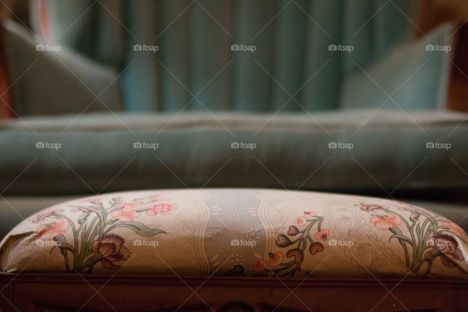 Floral footrest in front of antique  teal wingback chair from low perspective 