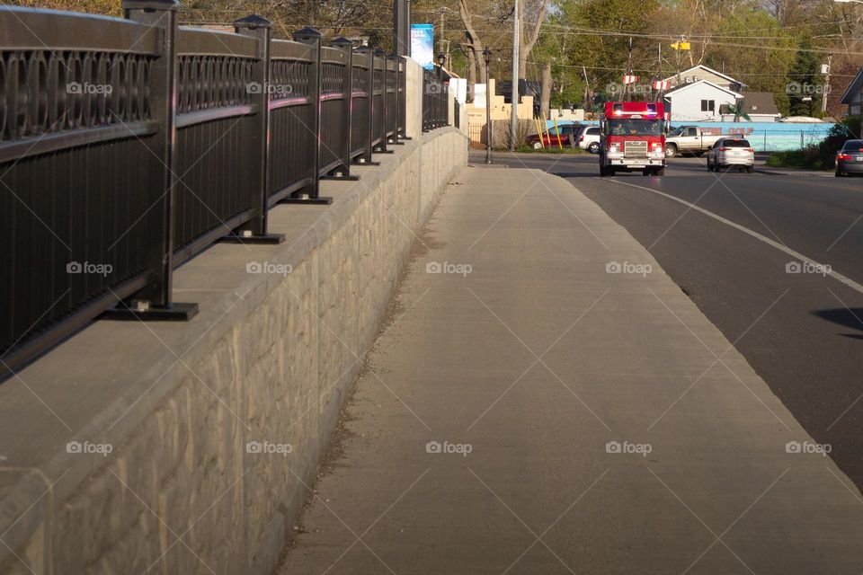 Bridge with sidewalk and wrought iron fence with a red fire truck in the background