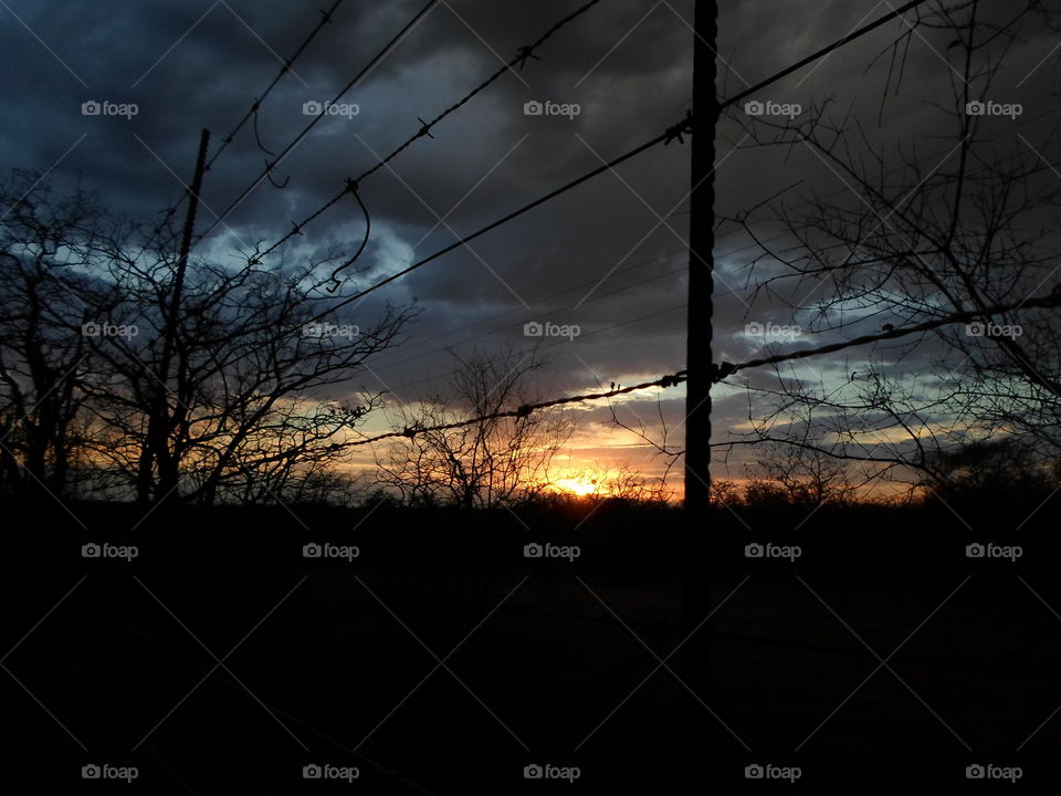 The sun rising through some barbed wire fence
