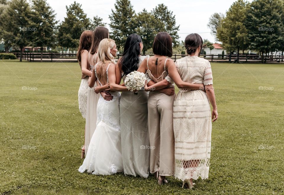 Rear view of bride and her bridesmaids posing for a photo on a lawn in park on wedding day