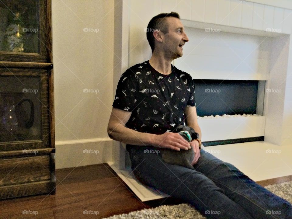 A man with his Boston Terrier pug mix sitting by the fireplace on a sunny day 