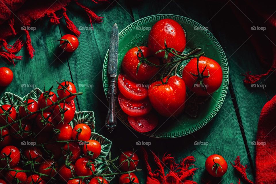 The vibrant red color of flamenco and cherry tomatoes is incredibly delicious, and they are presented on a green background with drops of water.