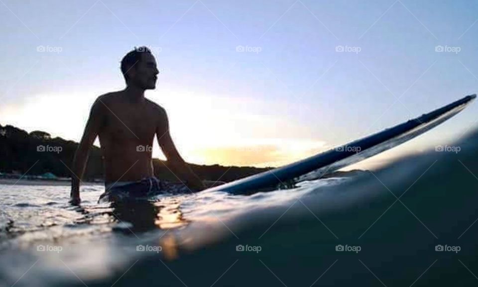Man sitting on surfboard at sea.