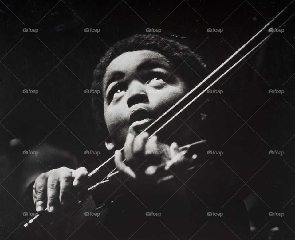 A young school boy plays his violin on stage during a recital.