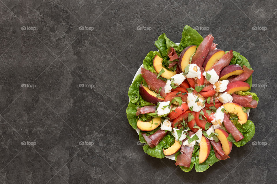 a colourful summer salad made with lettuce, tomatoes, yellow peaches, mozzarella cheese and ham.