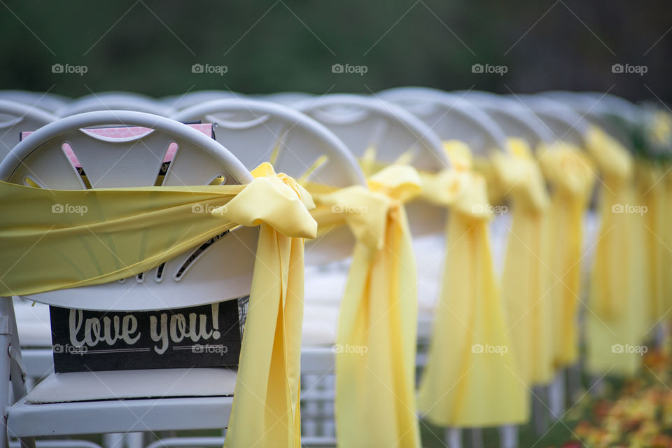 Rows of yellow bows and ribbons on white chairs at wedding ceremony