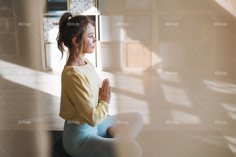 Young slender fitness blonde woman practice morning yoga near the window of home