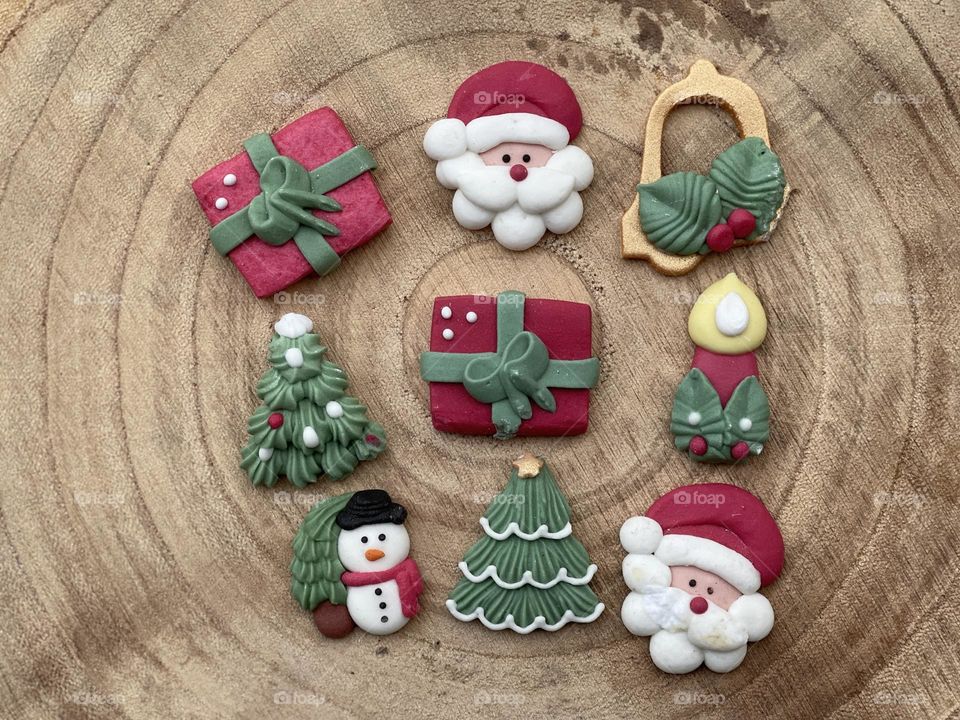 Christmas marzipan ornaments on a wooden board with a candle, snowman, santa claus, christmas tree, presents and christmas bell