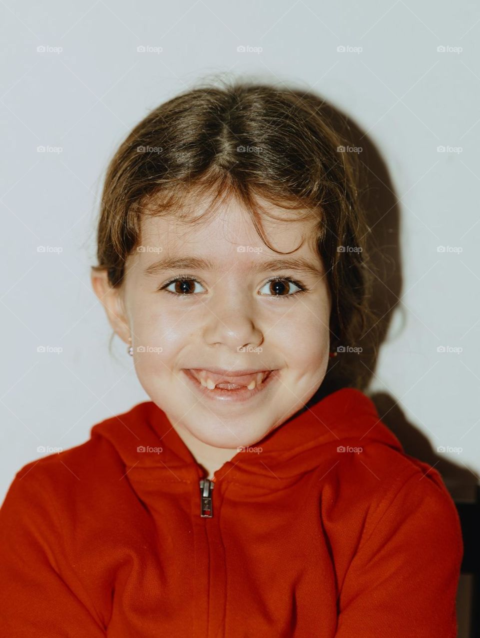 Portrait of one beautiful Caucasian brunette girl with a happy and toothless smile on her face on a white background with a hard shadow, close-up side view.