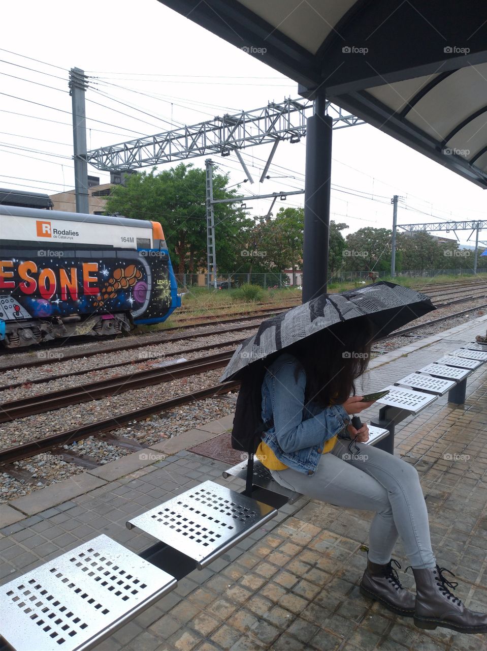 Estación de tren, chica con paraguas y móvil