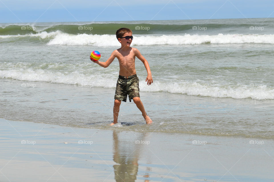 Young boy playing catch on the beach with waves in the background