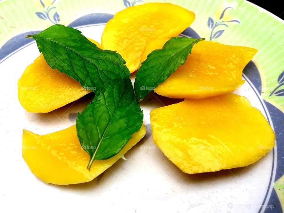 Mango fruits juicy pices and podina leafs on a plat.