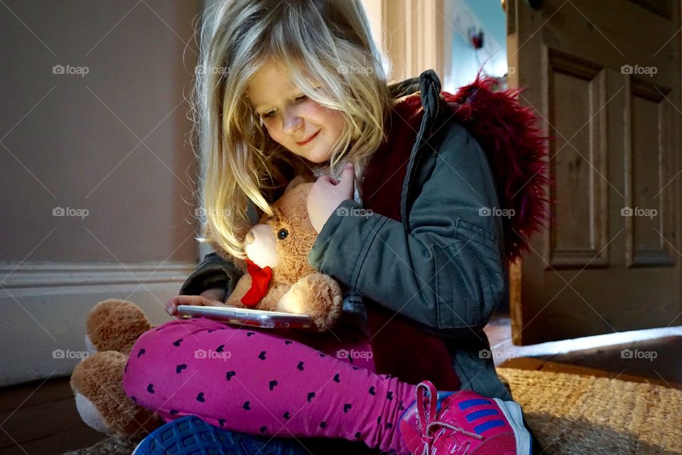 Girl holding teddy bear looking at cellphone